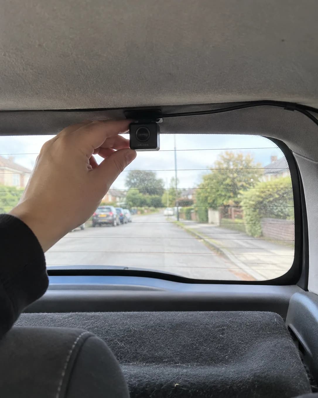The small Halden rear camera stuck inside the top of a hatchback rear window, its cable tucked into the headliner
