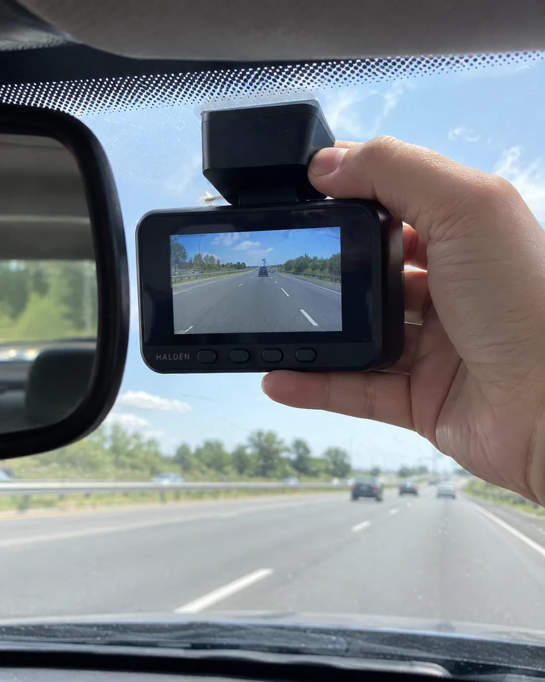 A hand pressing the Halden Duo 4K onto the windshield behind the mirror