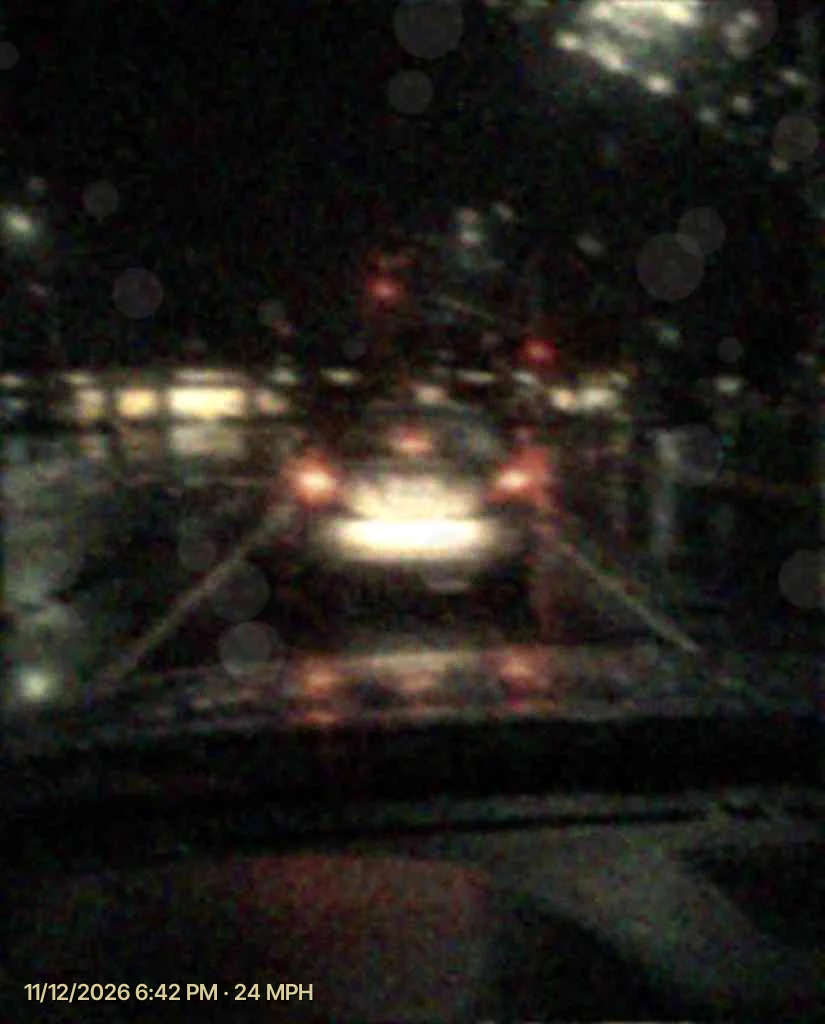 Night dash cam footage in the rain from a cheap camera, the plate of the car ahead a blur